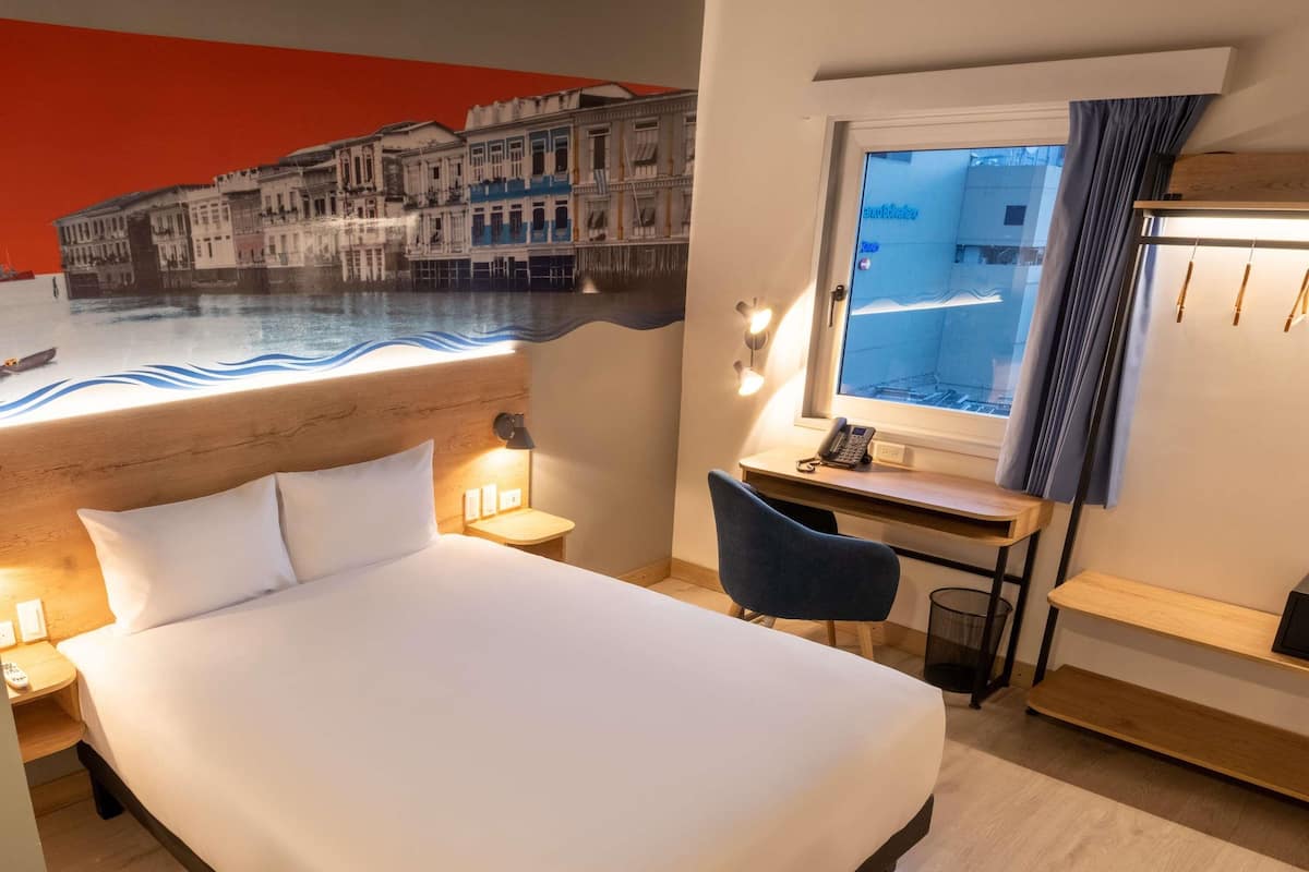 Habitació d'hotel amb llit, escriptori, cadira, làmpada d'escriptori, telèfon i finestra amb cortines.