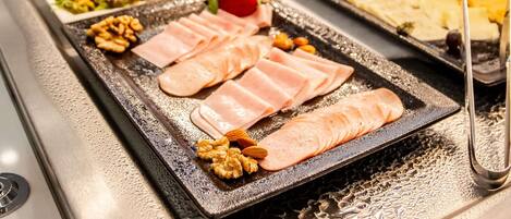 Un bufé con diversas opciones de comida, incluyendo carnes en rodajas y nueces.