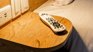 A wooden bedside table with a remote control, a lamp, and a power outlet. - Ibis Styles El Malecon Guayaquil (Guayaquil)