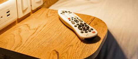 Una mesita de noche de madera con un control remoto, una lámpara y un enchufe.