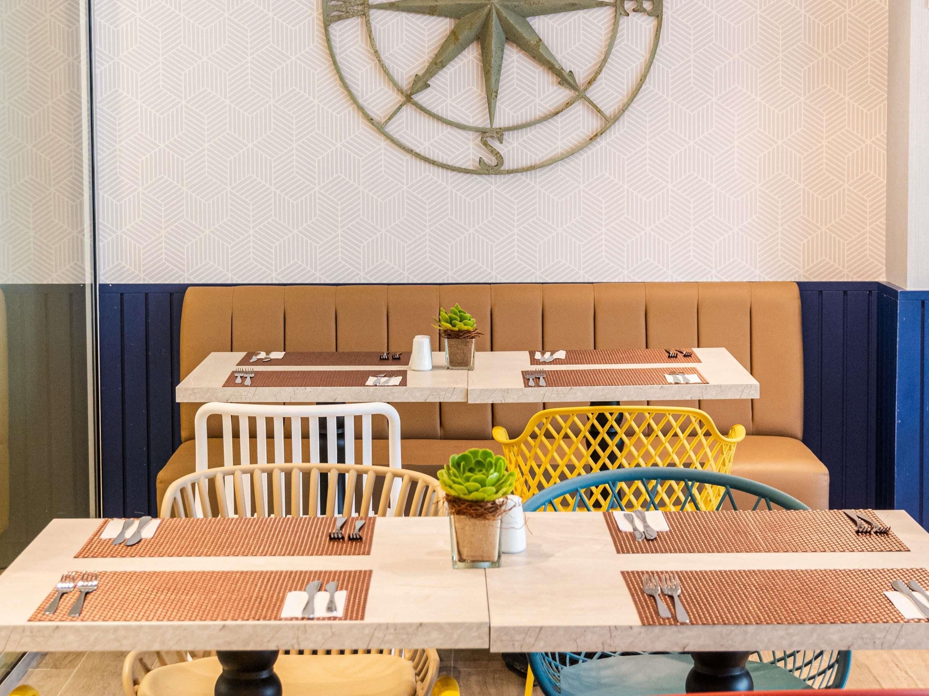 A dining area with a table set for two, a wall-mounted compass, and a patterned wall.