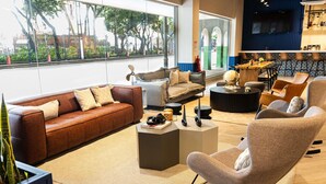 A modern living room with a brown leather sofa, a grey armchair, a coffee table, and a dining area with a wooden table and chairs. - Ibis Styles El Malecon Guayaquil (Guayaquil)