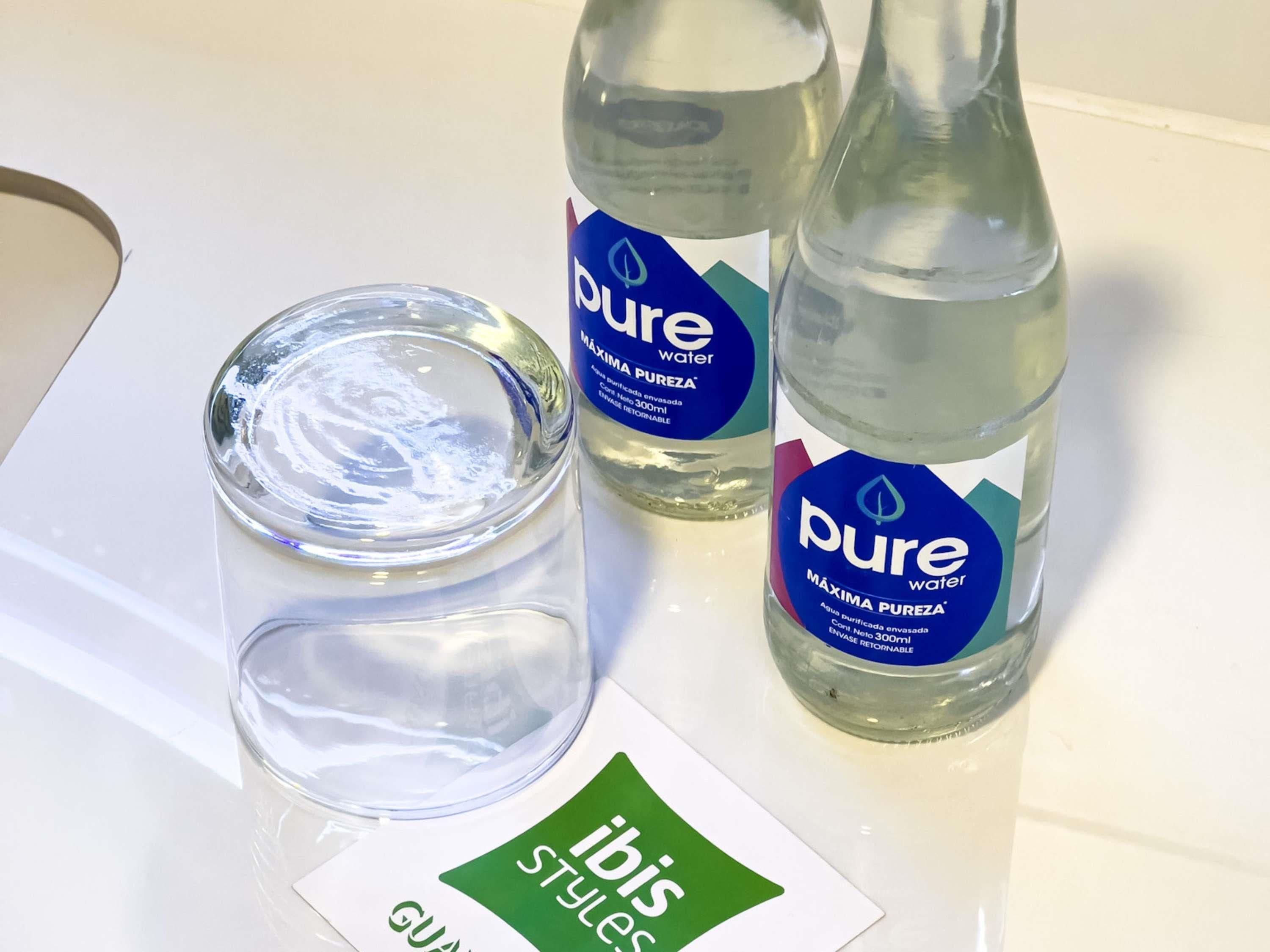 Duas garrafas de água Pure e um copo com tampa sobre uma superfície branca.