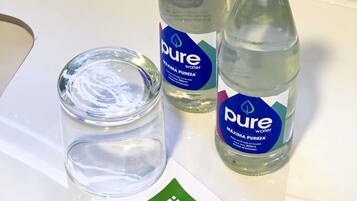 Duas garrafas de água Pure e um copo com tampa sobre uma superfície branca.