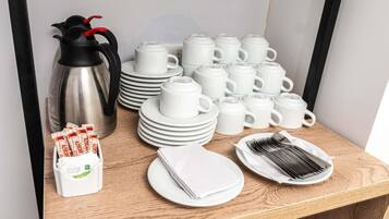 Uma mesa de madeira com uma composição organizada para o café da manhã, incluindo uma cafeteira, vários copos e pratos, e utensílios.