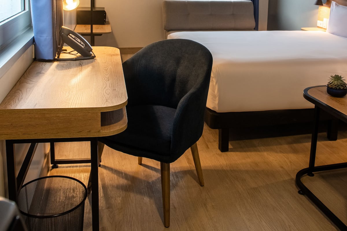 Una habitació d'hotel amb un llit, una taula amb una cadira, una finestra amb cortines i una vista del cel.