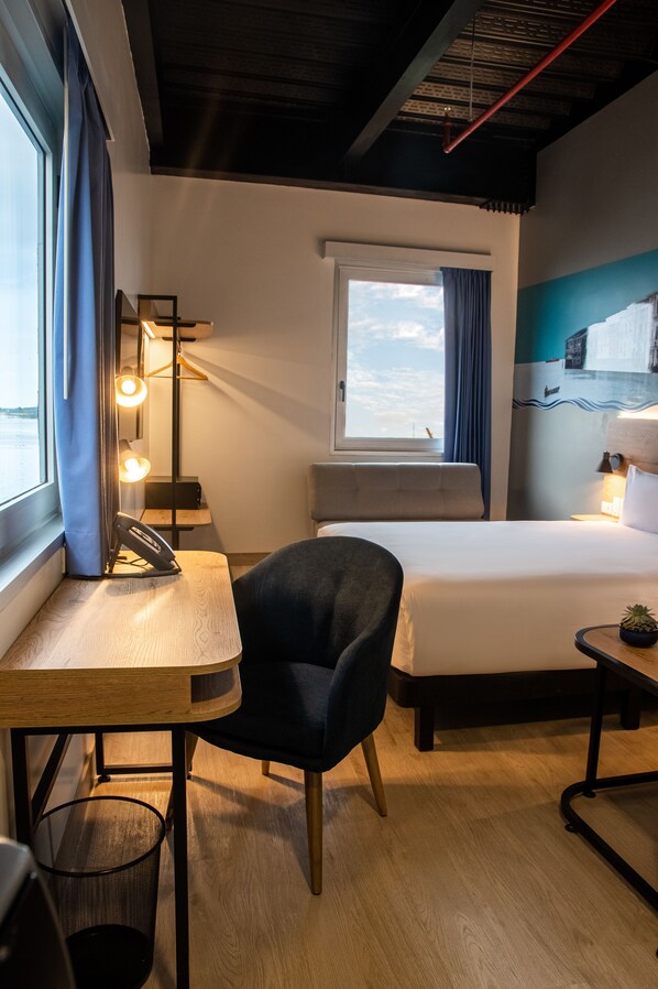 A hotel room with a bed, a desk with a chair, a window with curtains, and a view of the sky. - Ibis Styles El Malecon Guayaquil (Guayaquil)