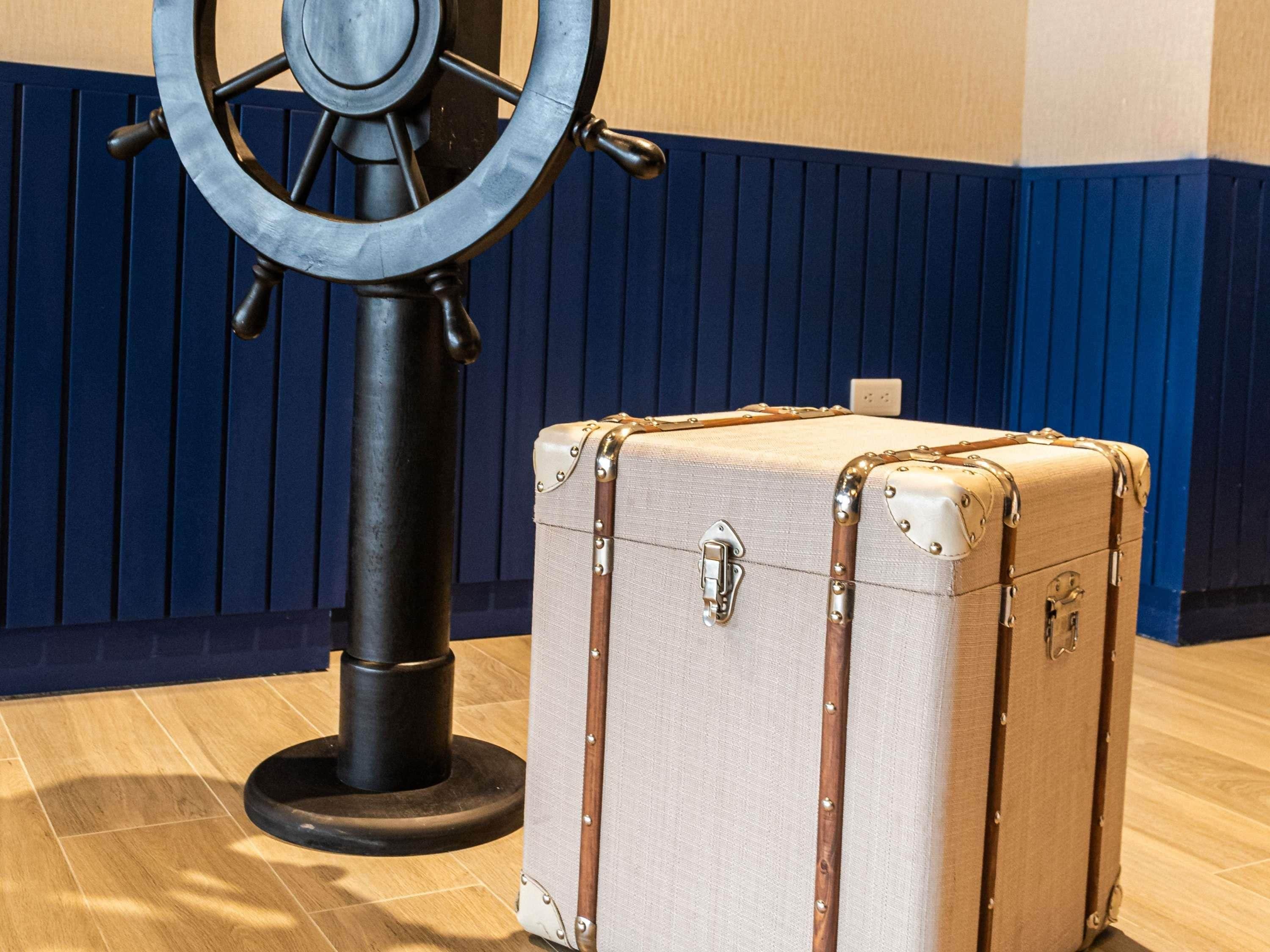 A vintage-style suitcase with metal rivets and a brass handle, placed next to a ship's wheel.