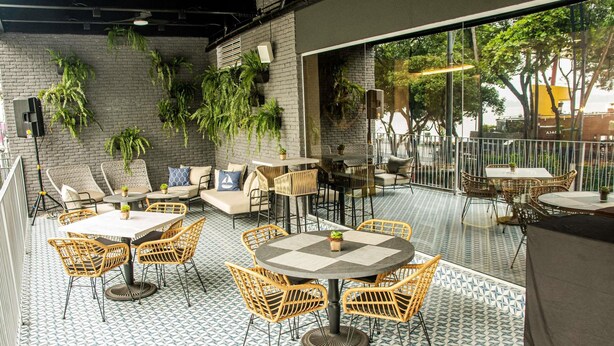 An outdoor seating area with tables and chairs, potted plants, and a view of trees through large windows. - Ibis Styles El Malecon Guayaquil (Guayaquil)