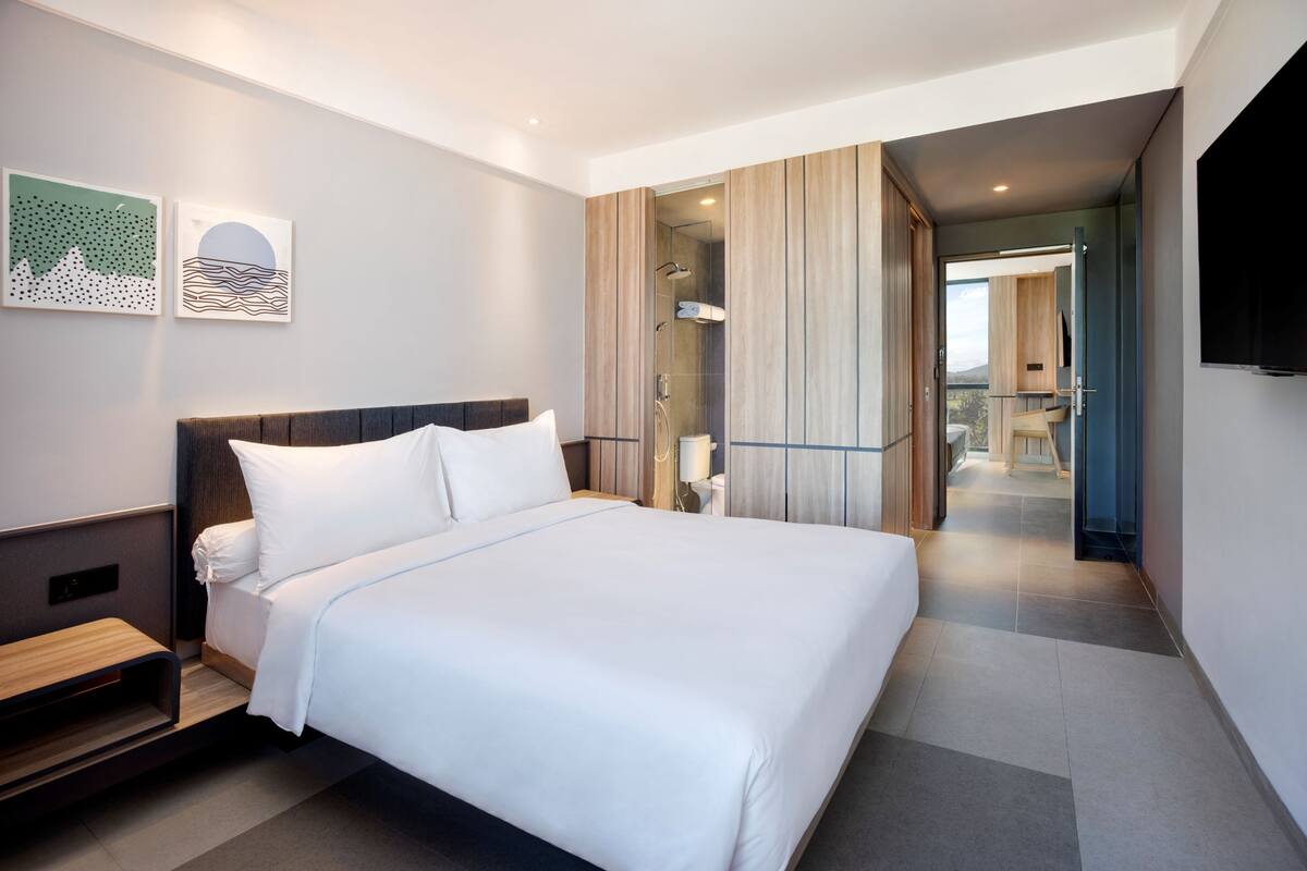A modern hotel room with a large bed, a walk-in closet, and a bathroom with a glass shower.