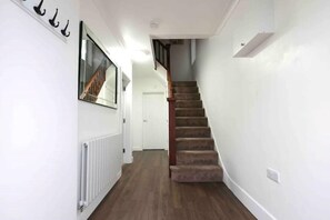 Staircase leads to a doorway at the end of a hallway with a radiator and hooks.