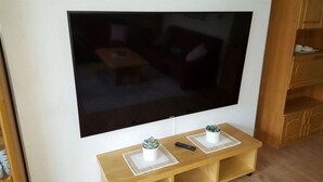 Een flatscreen televisie bevestigd aan een muur boven een houten tv-meubel, met twee afstandsbedieningen en een kleine potplant.