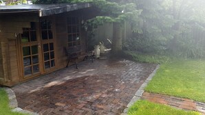 Een terras van bakstenen met een bank en een houten constructie met glazen deuren.