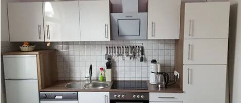 Una cocina compacta con armarios blancos, un lavamanos de acero inoxidable, una estufa y una cafetera.