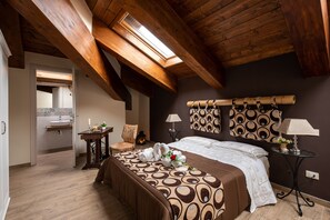 A bedroom with a sloped ceiling, a skylight, a bed with patterned bedding, a bedside table with a lamp, and a chair. - AGORA' CASTELNUOVO DELLA DAUNIA (Castelnuovo della Daunia)