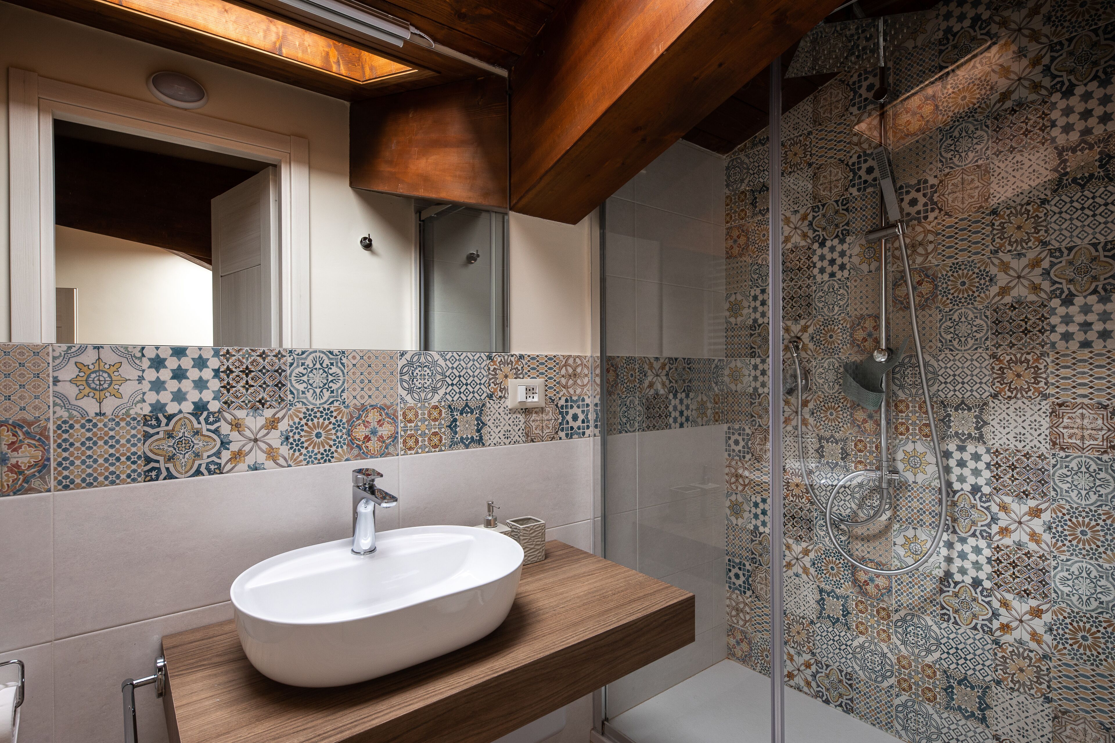 A bathroom with a white sink, wooden countertop, and a shower with patterned tiles.