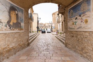 A cobblestone street with a stone archway, flanked by buildings with murals. - AGORA' CASTELNUOVO DELLA DAUNIA (Castelnuovo della Daunia)