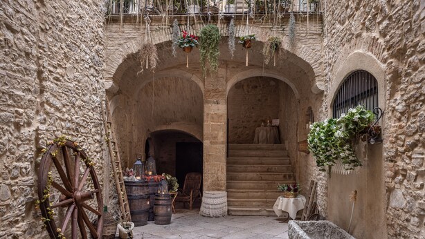 A stone courtyard with arched doorways, a wooden wheel, barrels, and hanging plants. - AGORA' CASTELNUOVO DELLA DAUNIA (Castelnuovo della Daunia)