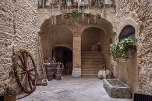 A stone courtyard with arched doorways, a wooden wheel, barrels, and hanging plants. - AGORA' CASTELNUOVO DELLA DAUNIA (Castelnuovo della Daunia)