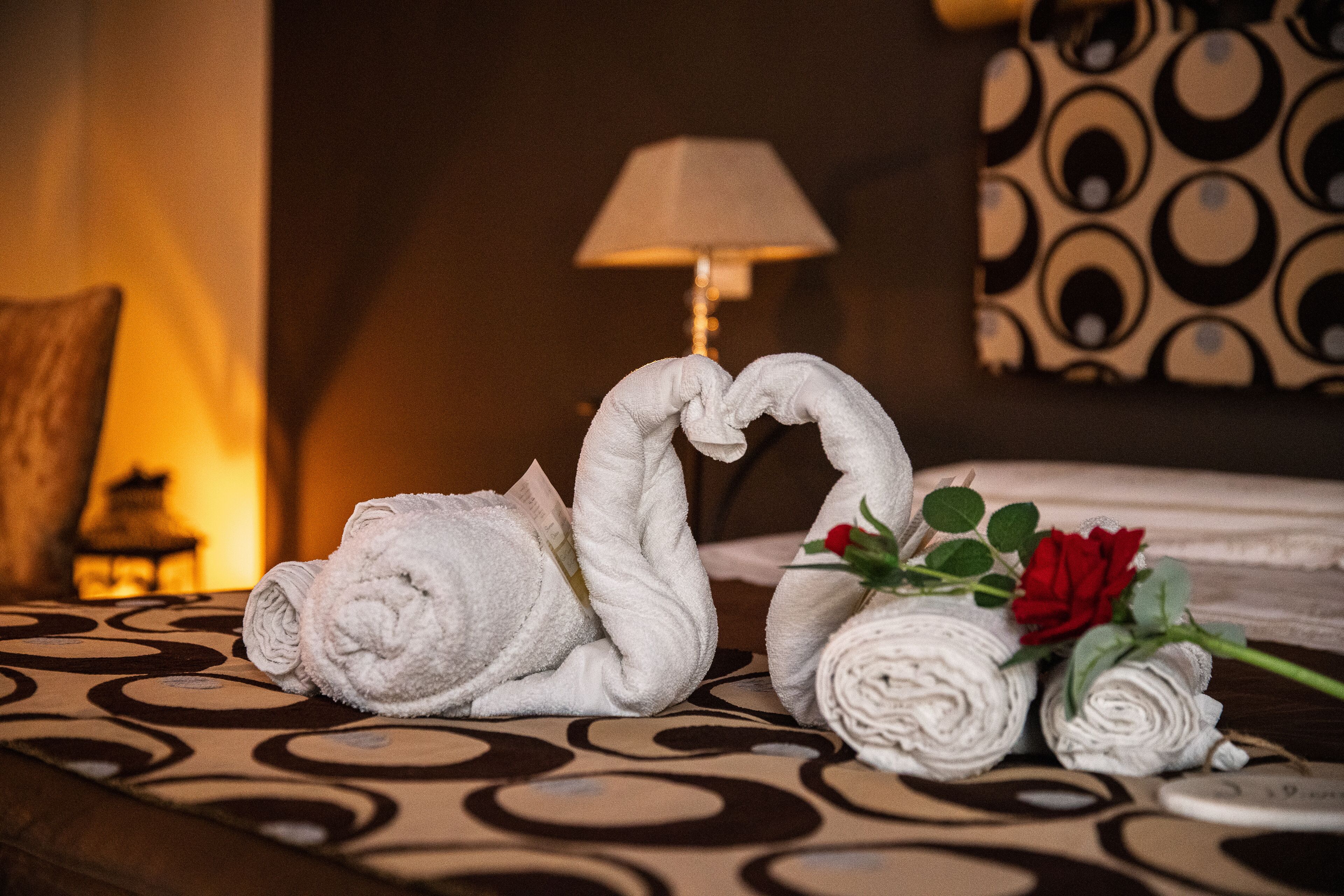 A hotel room with a bed, a lamp, and a decorative towel arrangement.