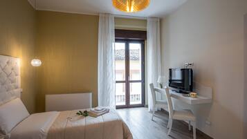 Habitación de hotel con cama, escritorio con televisor y vista a través de un ventanal.