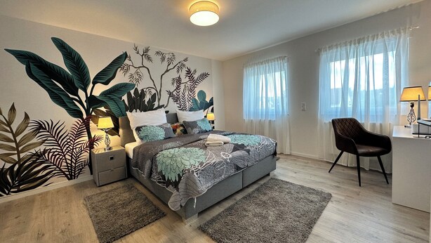 A modern bedroom with a bed, nightstands, a desk, and a chair.