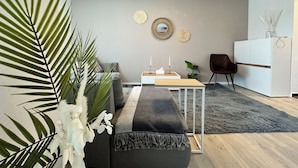 A modern living room with a sofa, a coffee table, a dining table, and a small kitchen area.