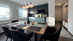 A modern kitchen with a dining area, featuring a wooden table, black chairs, and pendant lights.