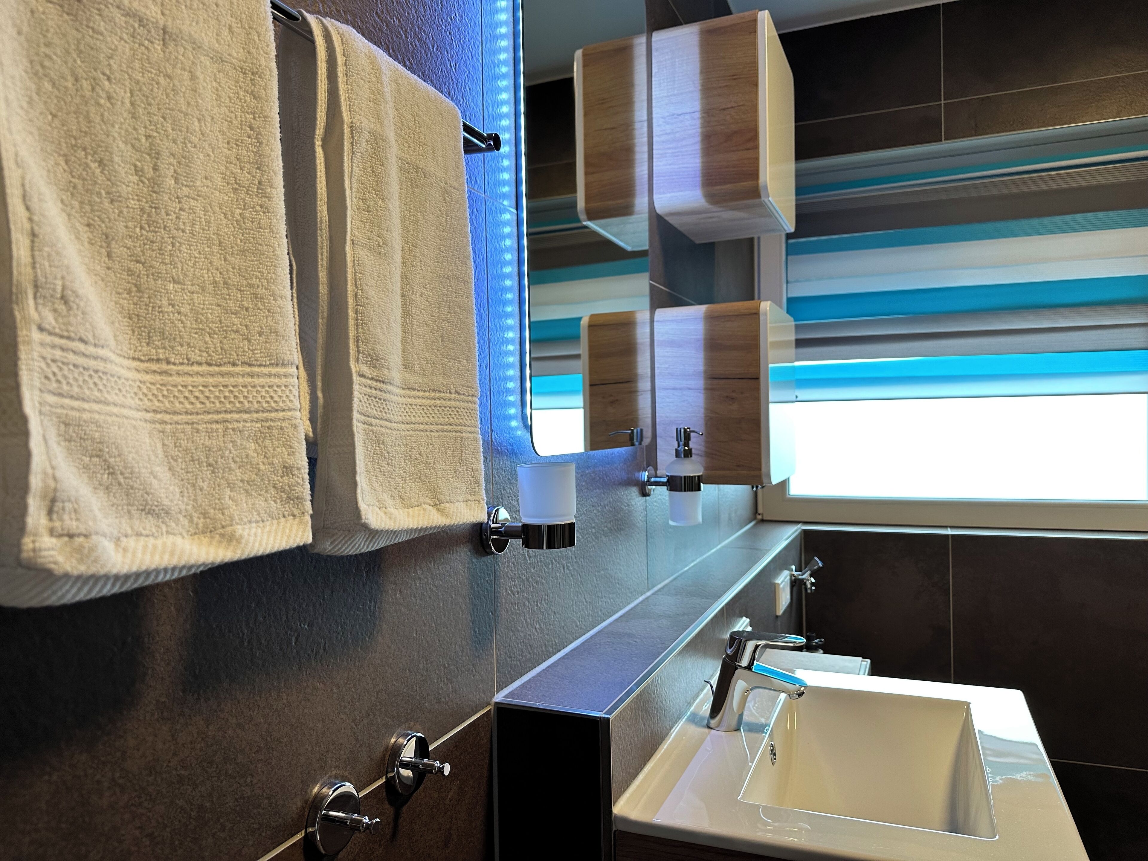 A modern bathroom with a large mirror, a sink, and two towel dispensers.
