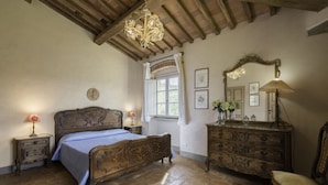 Een slaapkamer met een houten bed, een kaptafel, een stoel, een raam met gordijnen en een kroonluchter.