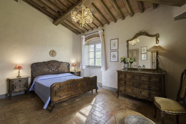 Un dormitorio con una cama de madera, un aparador, una silla, una ventana con cortinas y una araña.