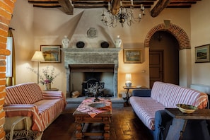 Ein traditionell eingerichteter Raum mit Kamin, zwei Sofas, einem Tisch und einer Kristallleuchter.