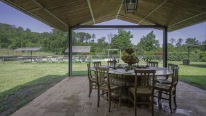Een terras buiten met een houten tafel en stoelen, omgeven door een tegelvloer en een houten pergola.