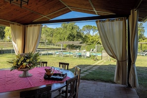 An outdoor dining area with a table set for two, a wicker basket with flowers, and a view of a pool and garden. - Leopolda In Selvarella By Geco Vacation Rentals (Bucine)
