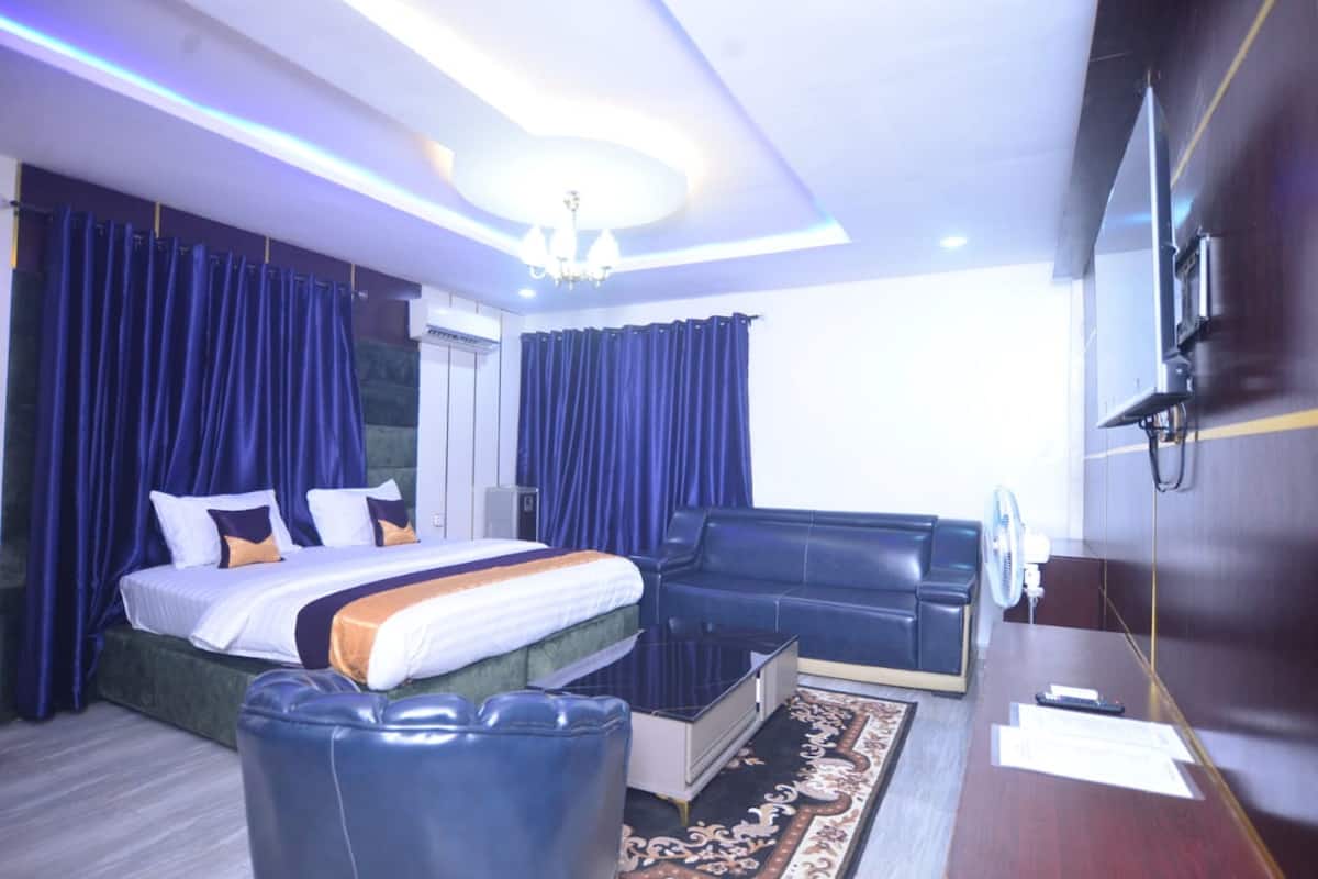 A modern hotel room with a large bed, a sofa, a desk, and a chandelier.