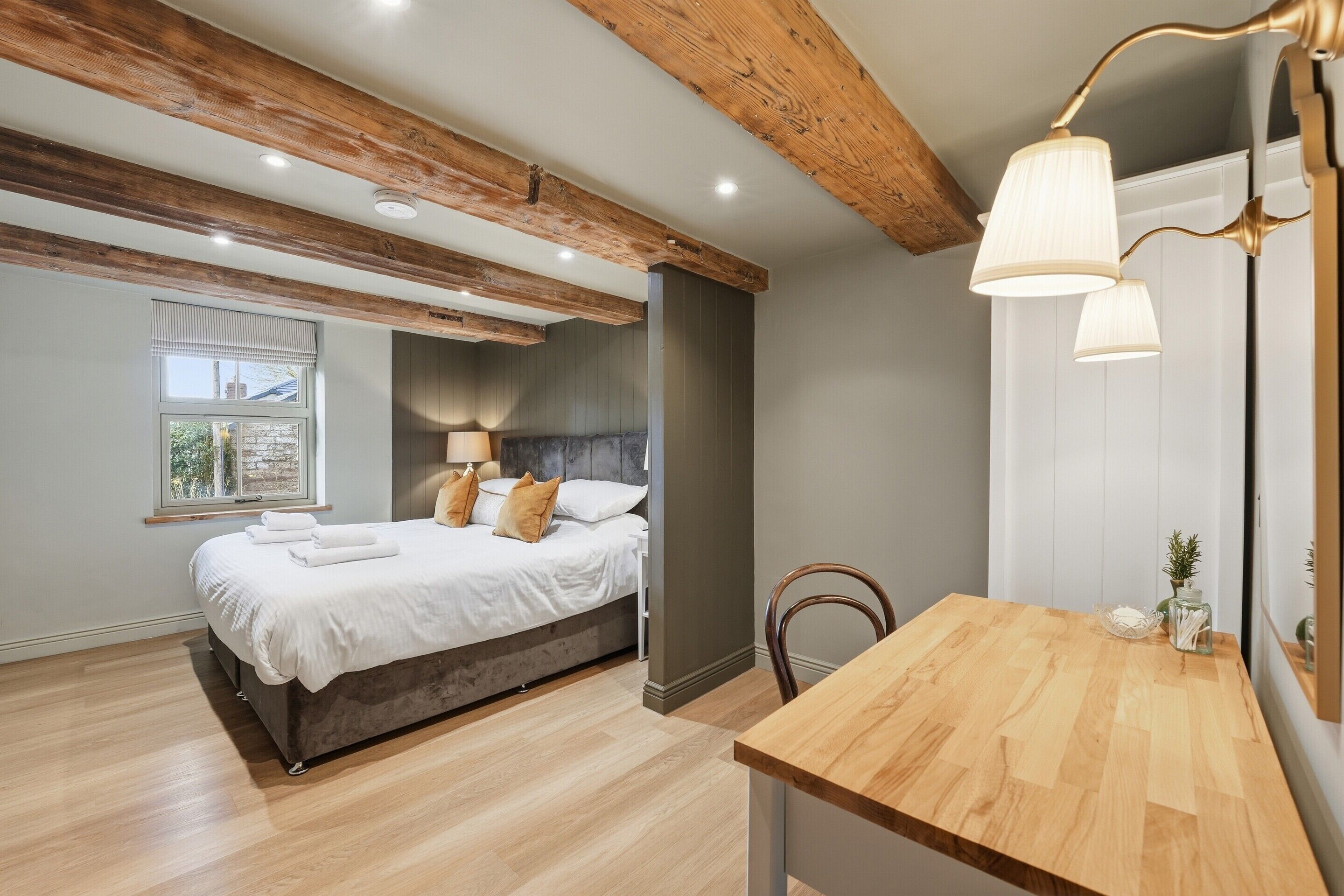 A bedroom with a wooden ceiling, a bed with white linens, a bedside table, and a mirror.