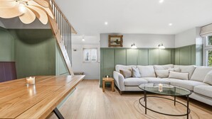 A modern living room with a wooden dining table, a glass coffee table, and a green upholstered sofa. - Laburnum Cottage (Tarporley)