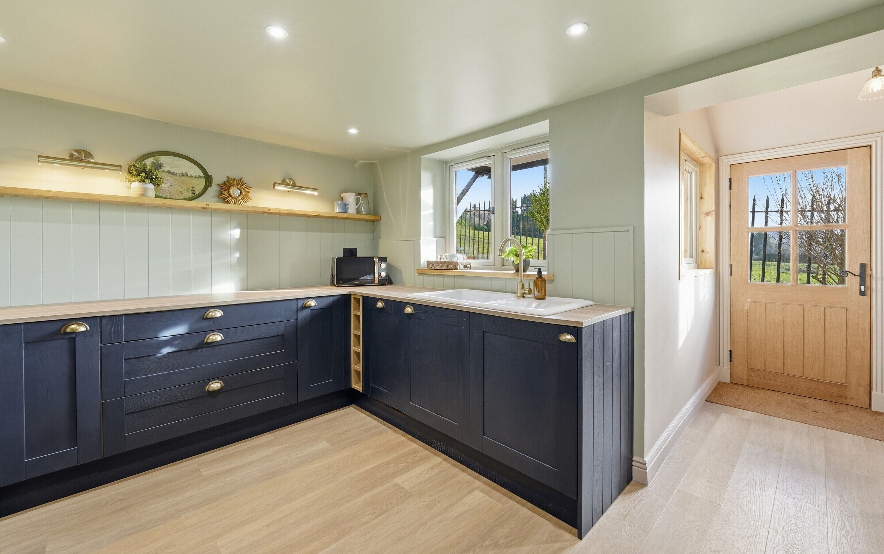 A kitchen with dark cabinetry, a wooden countertop, and a window with a view of greenery.