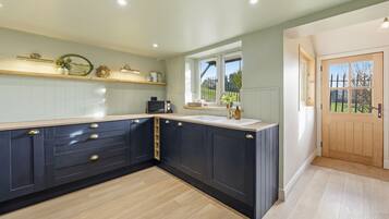 A kitchen with dark cabinetry, a wooden countertop, and a window with a view of greenery.