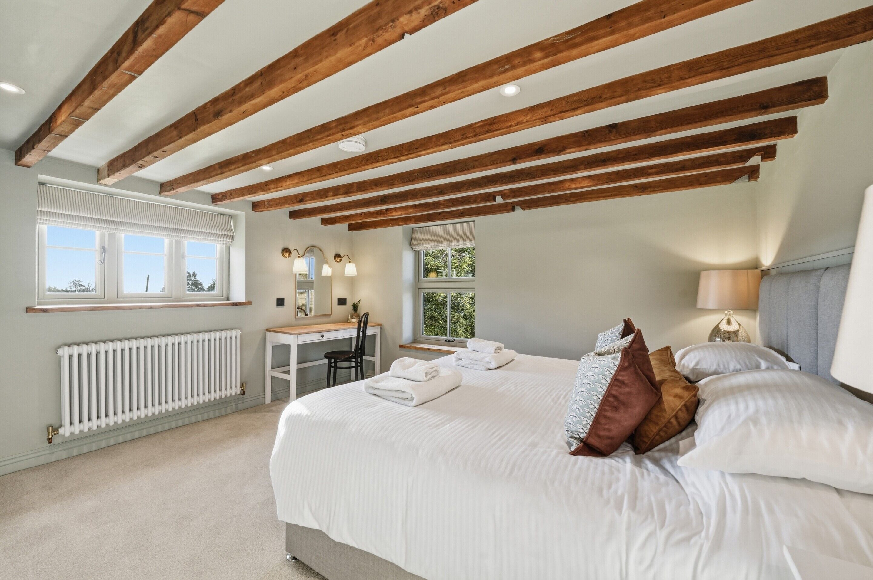 A bedroom with a large bed, wooden beams, a desk, and a window.