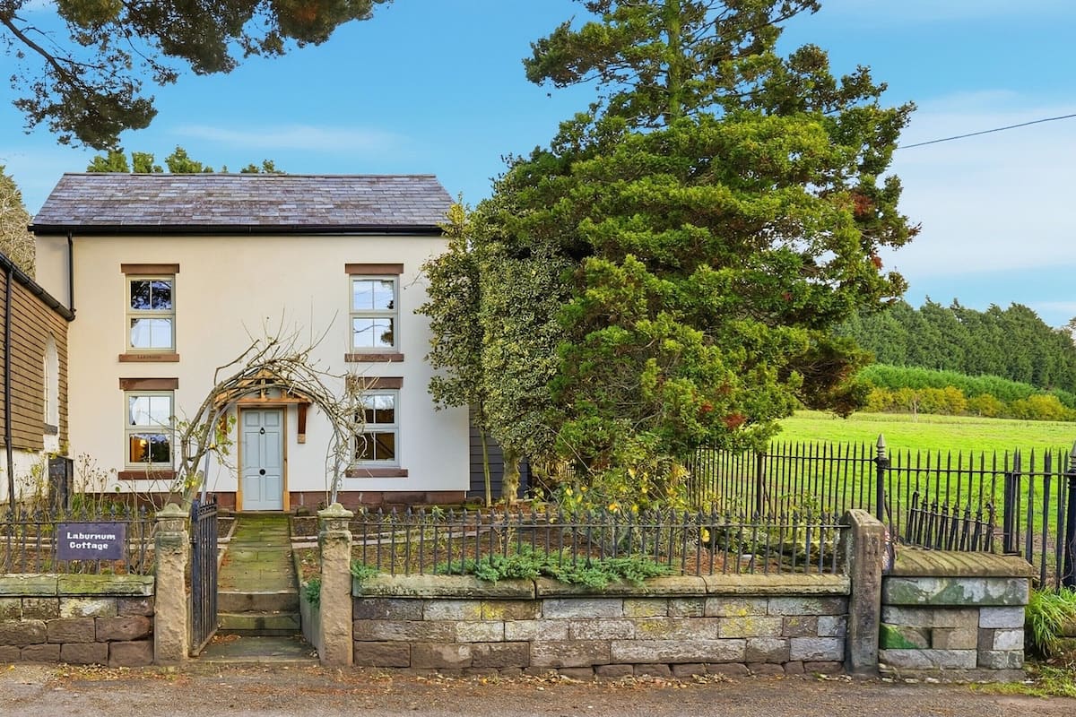 A two-story building with a stone entrance, a sign reading "Laburnum Cottage," and a black metal fence.
