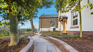 A pathway leading to a building with a brick wall and a window. - Laburnum Cottage (Tarporley)