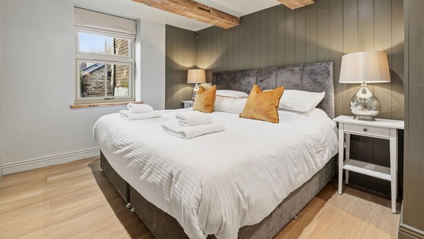 A modern bedroom with a large bed, two bedside tables, a window with blinds, and wooden beams on the ceiling. - Laburnum Cottage (Tarporley)