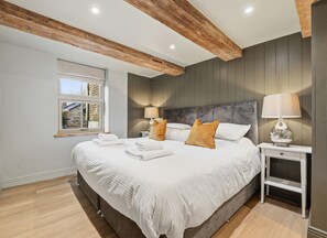 Ein modernes Schlafzimmer mit einem großen Bett, zwei Nachttischen, einem Fenster mit Jalousien und Holzbalken an der Decke.