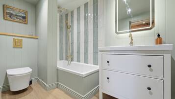 A bathroom with a white toilet, a bathtub, a vanity with drawers, a mirror, and a framed picture on the wall.