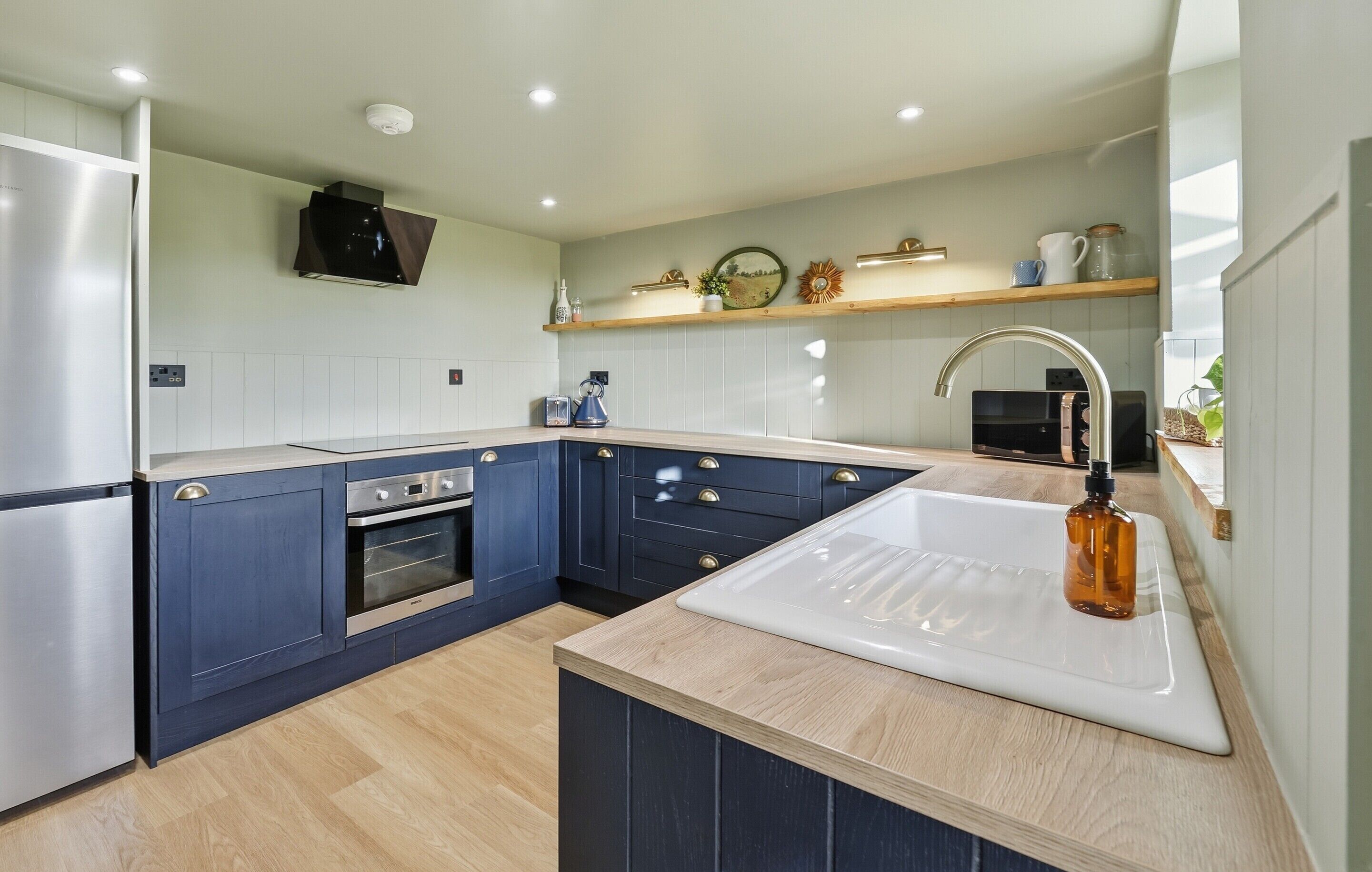 A modern kitchen with a built-in oven, a stainless steel refrigerator, and a white sink.