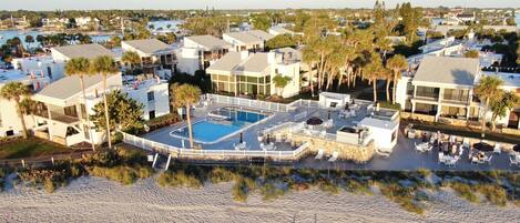 Et resort med pool i centrum, flere bygninger og en strand.