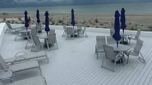 Een terras met buitenmeubelen en parasols met uitzicht op een strand.