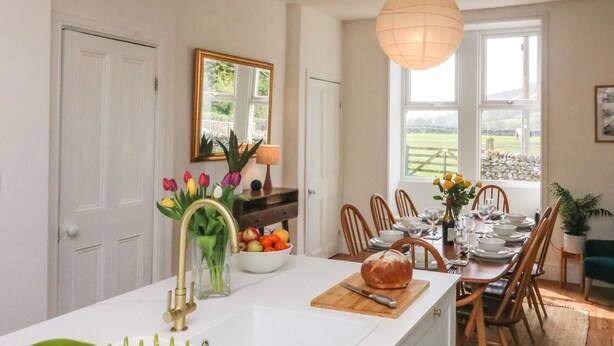 Cozinha moderna com ilha central, área de jantar com cadeiras de madeira e vista para o exterior.