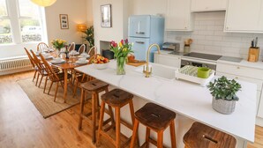 Uma cozinha moderna com armários brancos, uma geladeira azul e uma área de jantar com cadeiras de madeira e uma mesa branca.